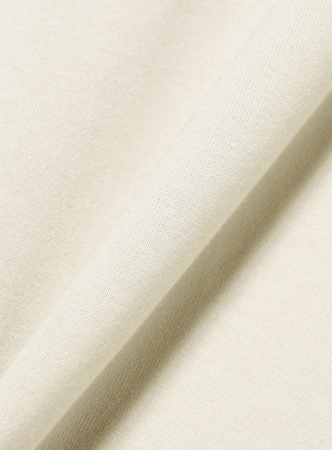 A close-up of light beige fabric reveals a soft, smooth texture with a visible diagonal fold, highlighting the material’s fine weave and natural drape—ideal for crafting the TTT MSW Wave Logo Ringer T-Shirt or elevating everyday streetwear essentials.