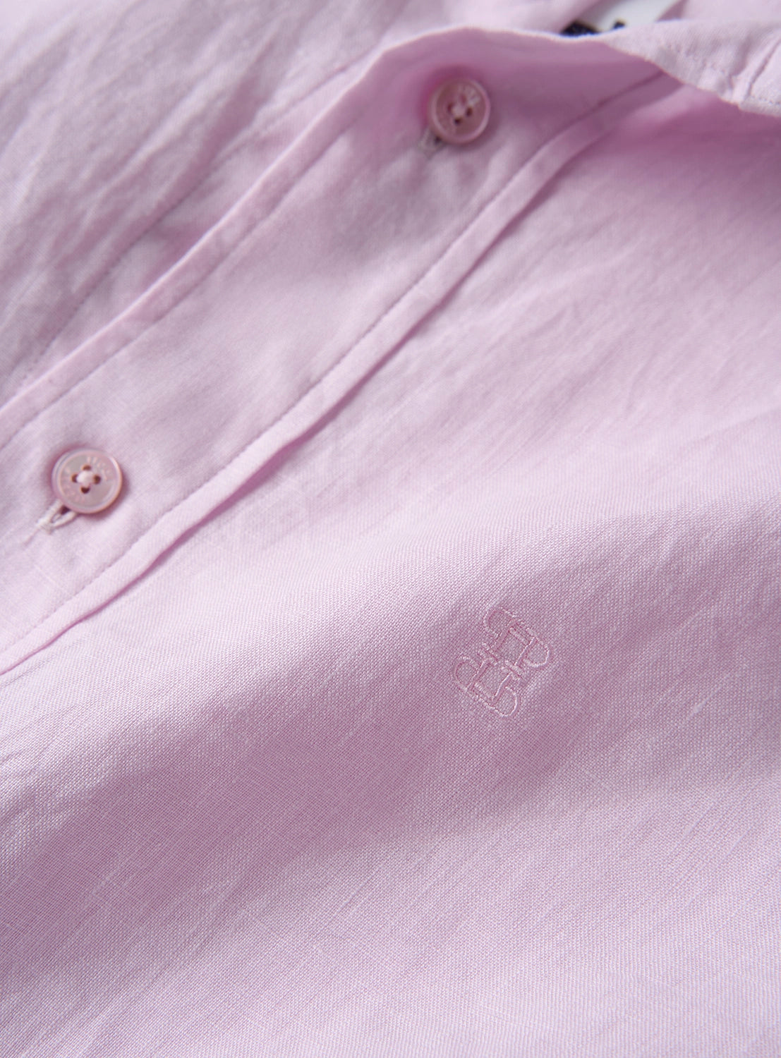 Close-up of a baby pink shirt with button details and a logo.