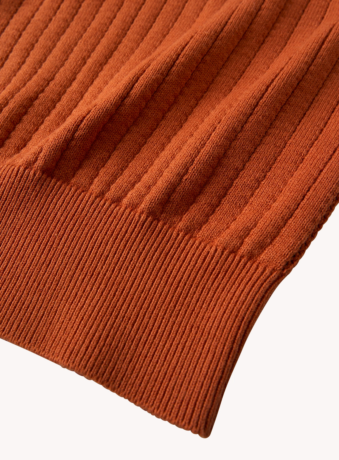 Close-up of rust-colored ribbed knit vest fabric, detailing the vertical ribbing and hem texture.