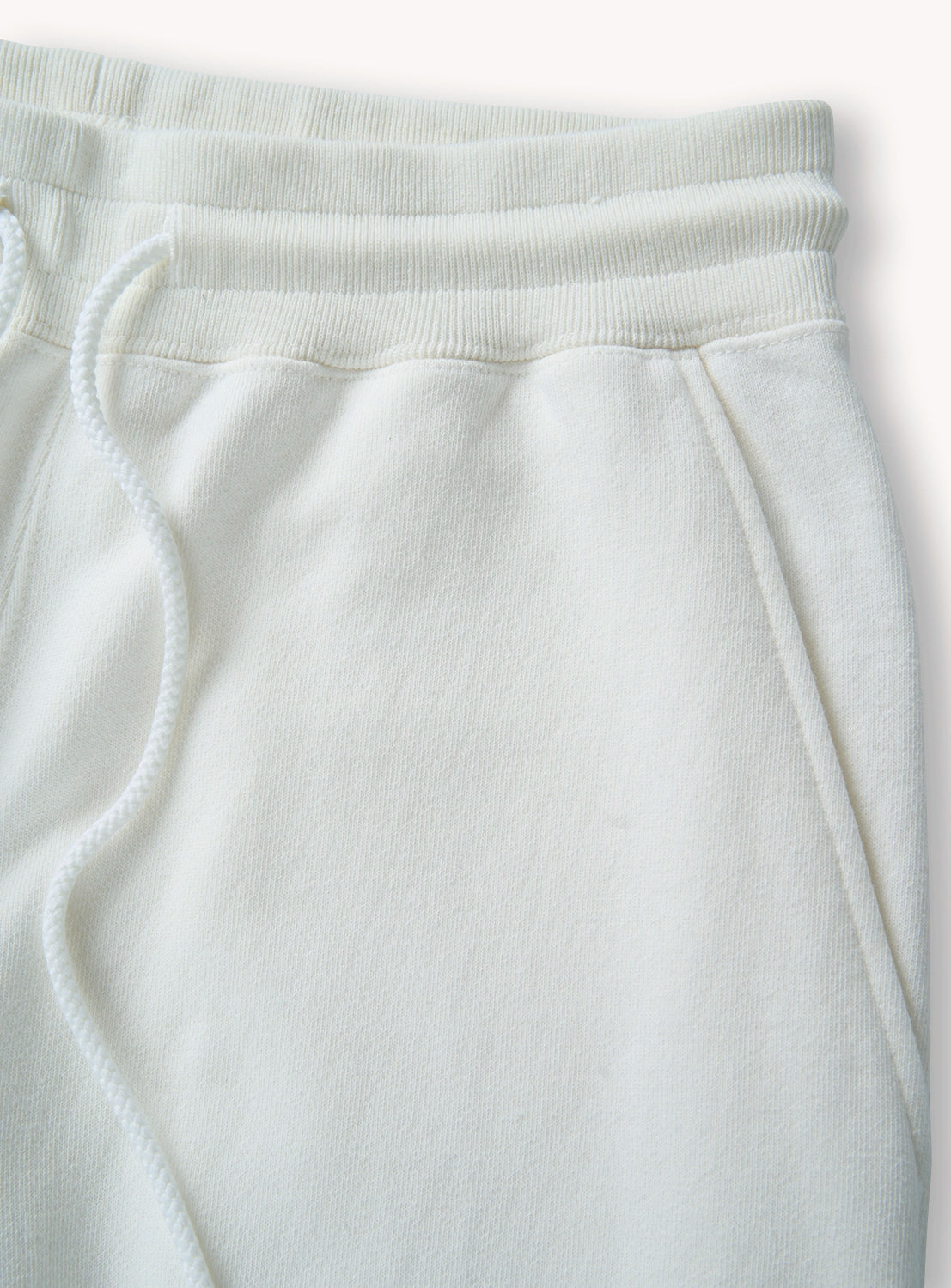 Close-up of white sweatpants featuring the drawstring and pocket detail. 