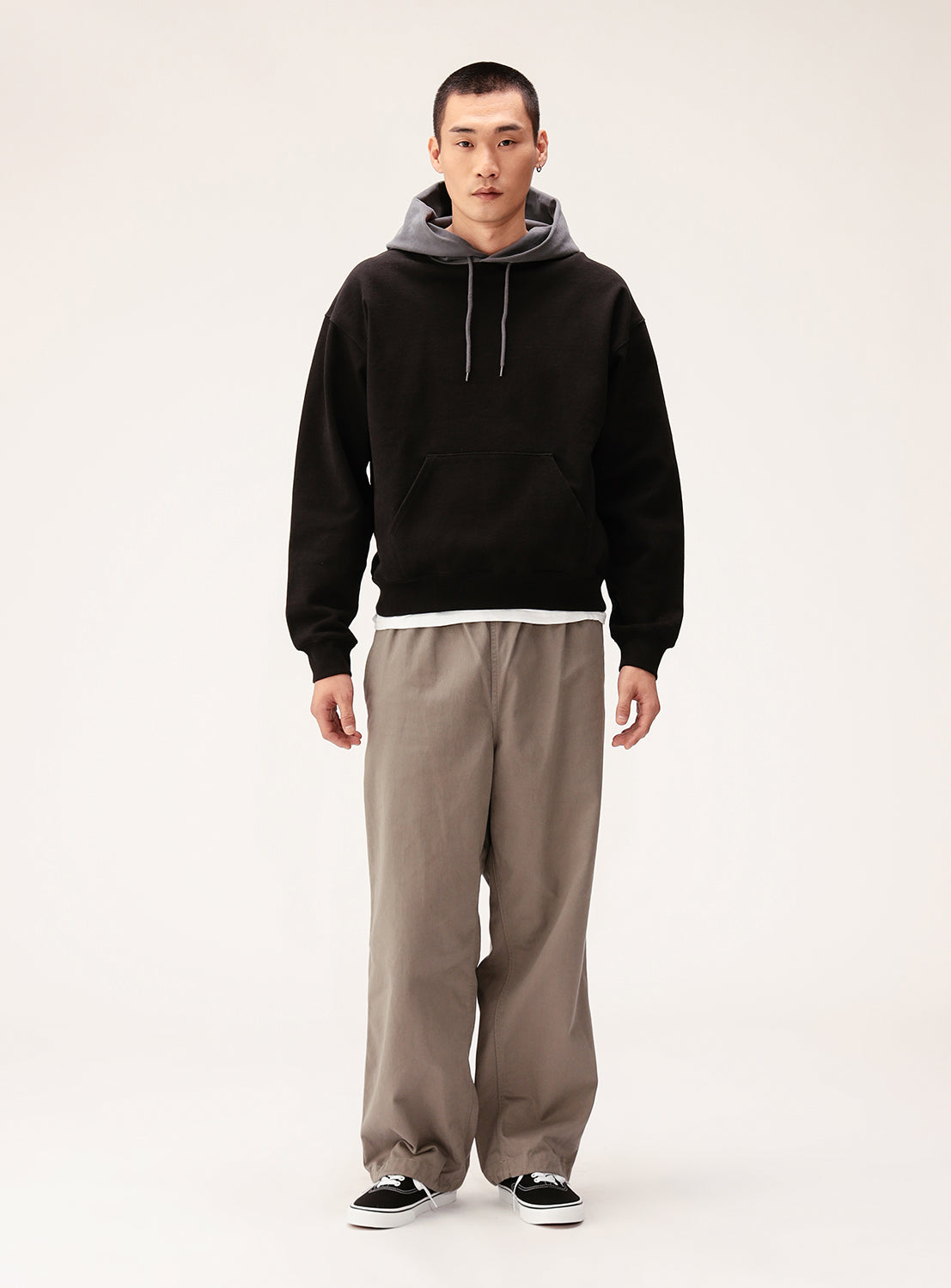 A person faces forward against a plain light background, wearing the BEAMS Color Block Heavyweight Fleece Hoodie with a gray hood, loose beige pants, black-and-white sneakers, and a white shirt peeking out at the hem.