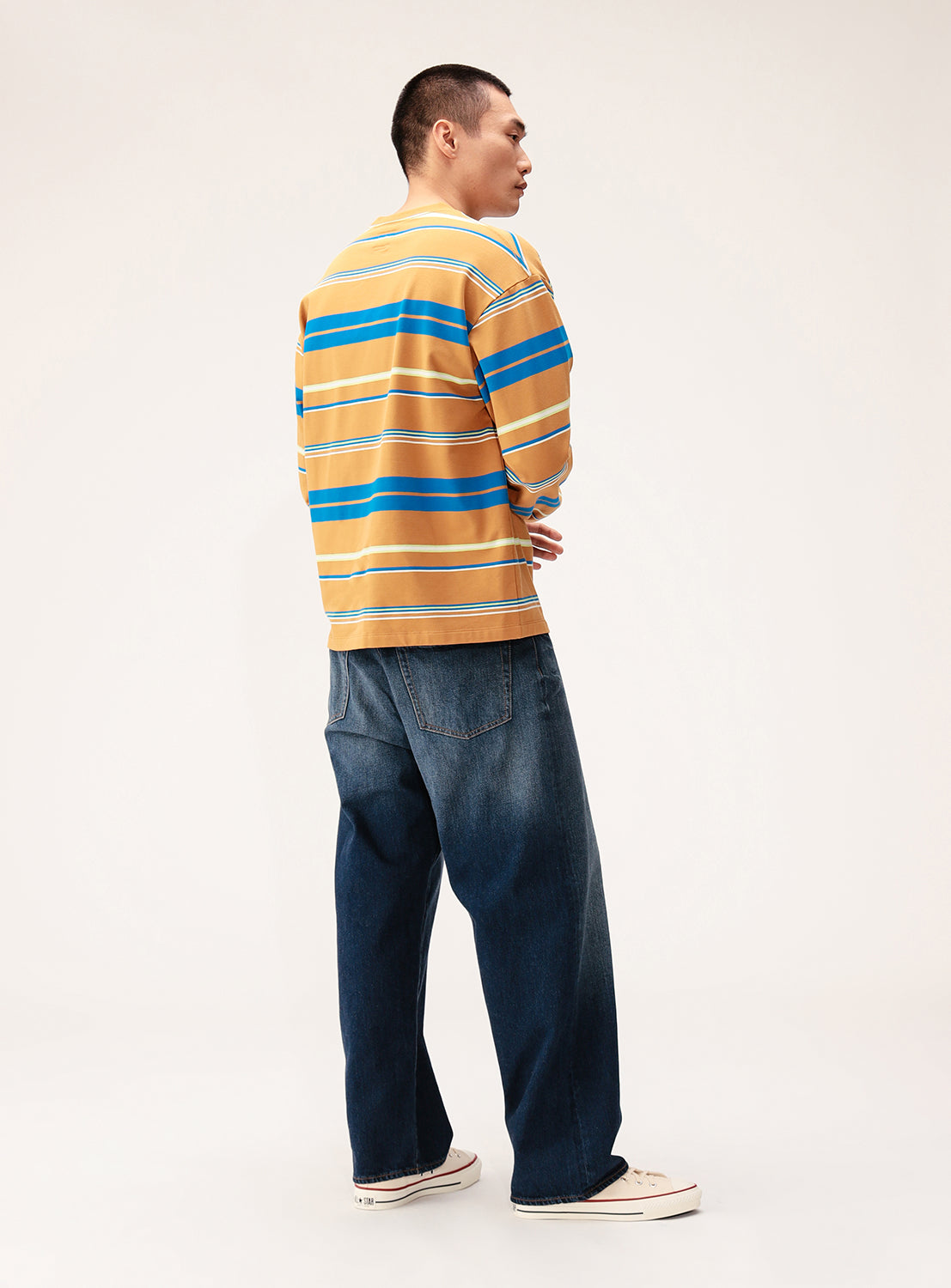 A person faces away wearing the BEAMS Multi-Stripe Crew Neck Wide Fit Sweatshirt, loose blue jeans, and white sneakers, styled effortlessly against a plain light background.