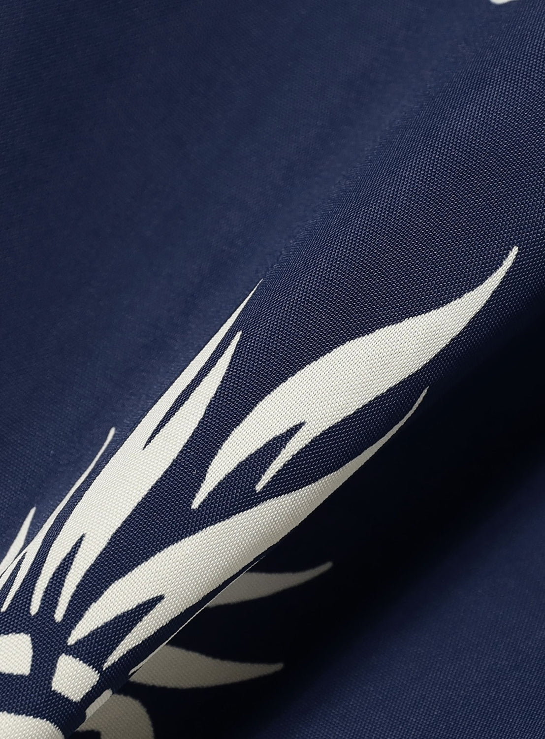 Close-up of the SUN SURF Exclusive Patchwork Aloha Shirt 26SS: dark blue fabric features a white abstract floral or leaf pattern, reminiscent of vintage aloha shirts, with gentle folds creating subtle shadows and highlights.