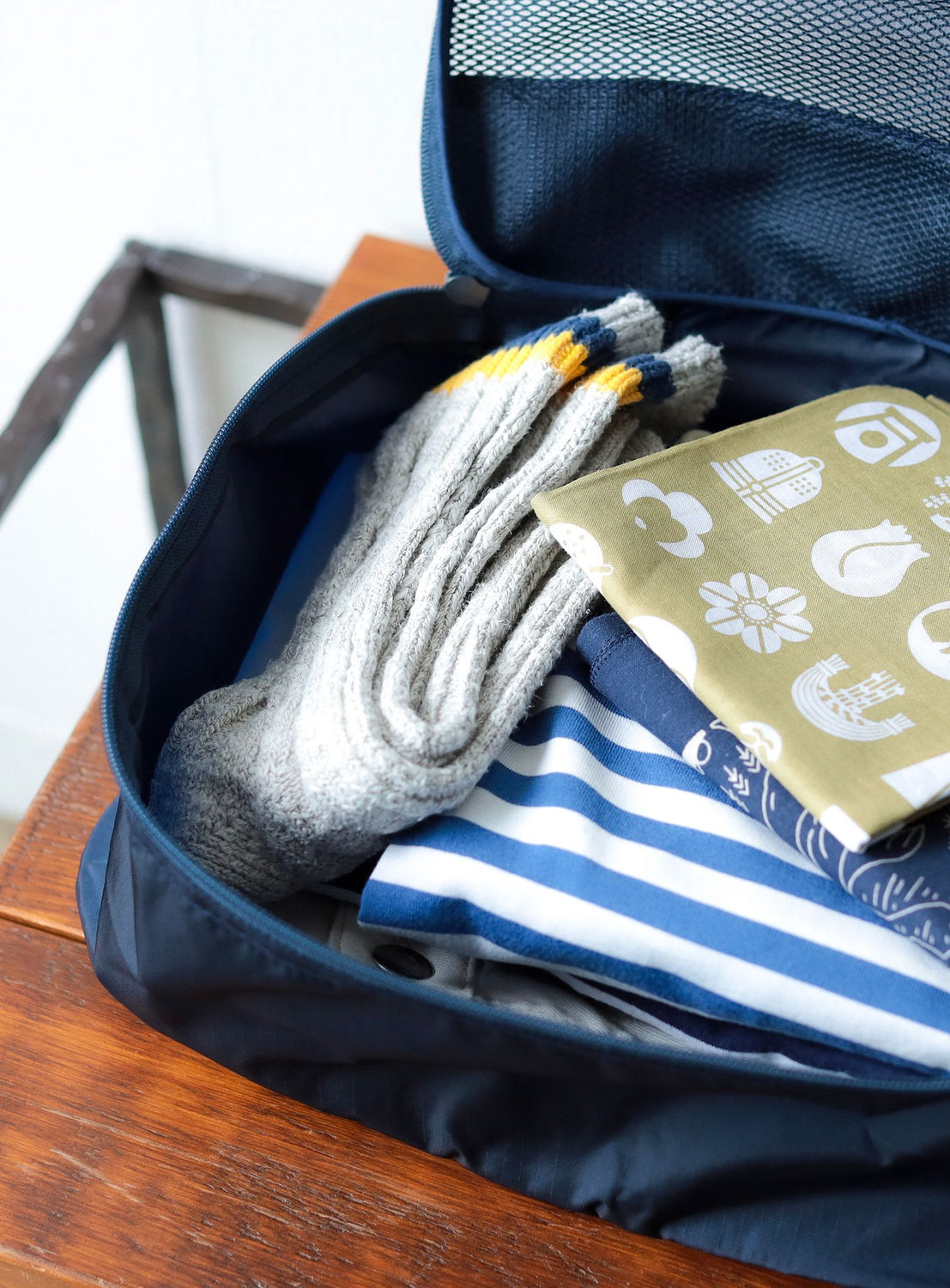 Navy blue travel bag with folded clothes and socks on a wooden surface