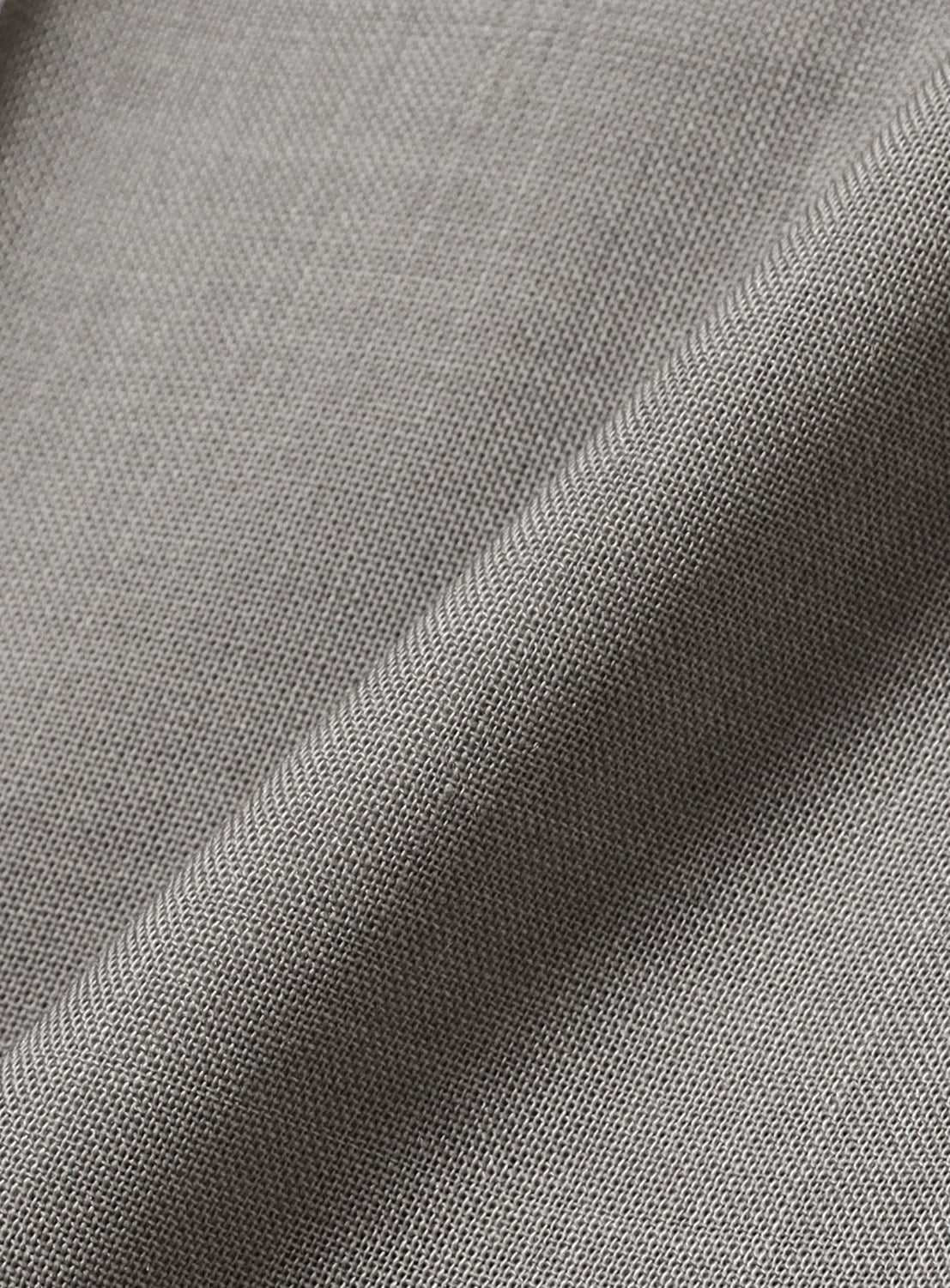 Close-up of KANAKO SAKAI Sheer Trousers in light gray, featuring fine textured woven fabric and a diagonal fold that accentuates the detailed weave pattern and tailored look along the crease.