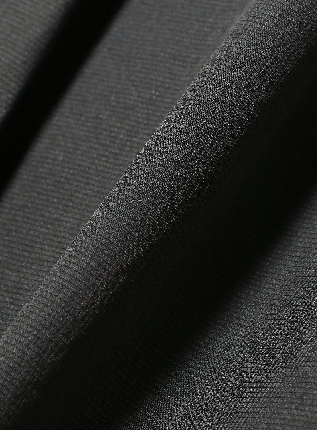 Close-up of the BEAMS Two-Pleat Wide Tapered Trousers in black, featuring breathable fabric with a subtle grid pattern and a soft, smooth finish. A visible fold runs diagonally across the material.