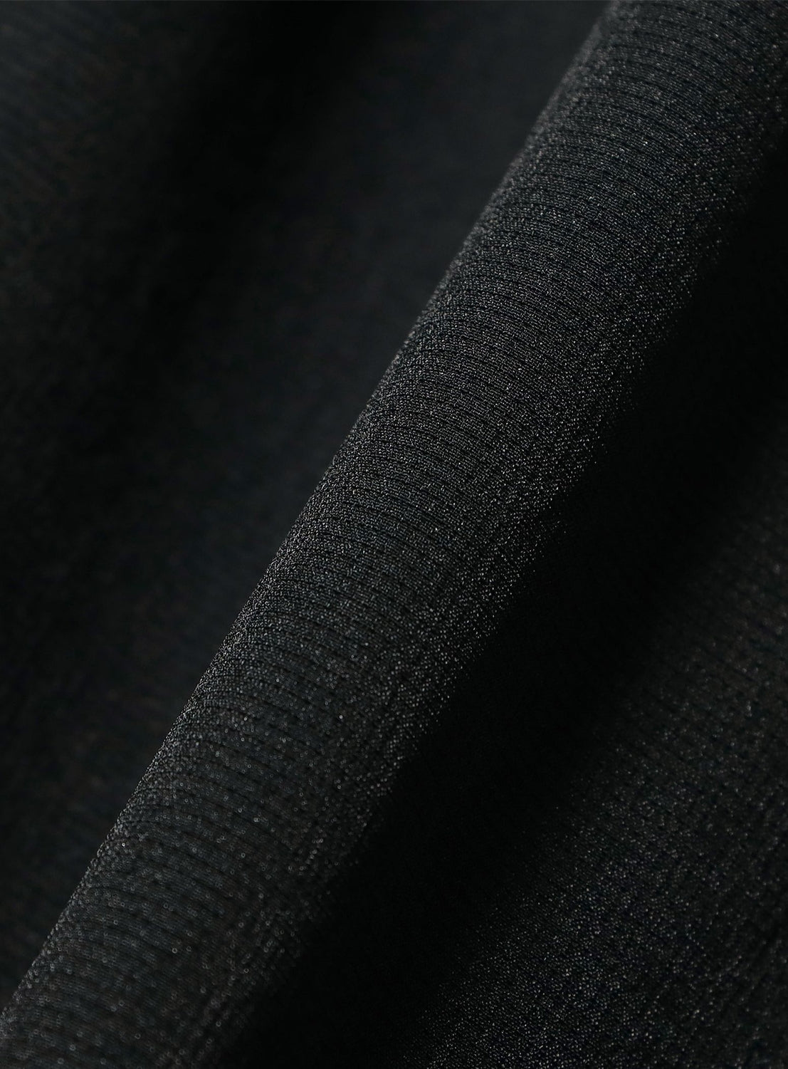 Close-up of BEAMS Two-Pleat Wide Tapered Trousers in black, highlighting the textured mesh-like fabric with visible weave and soft folds, plus a diagonal seam across the material.