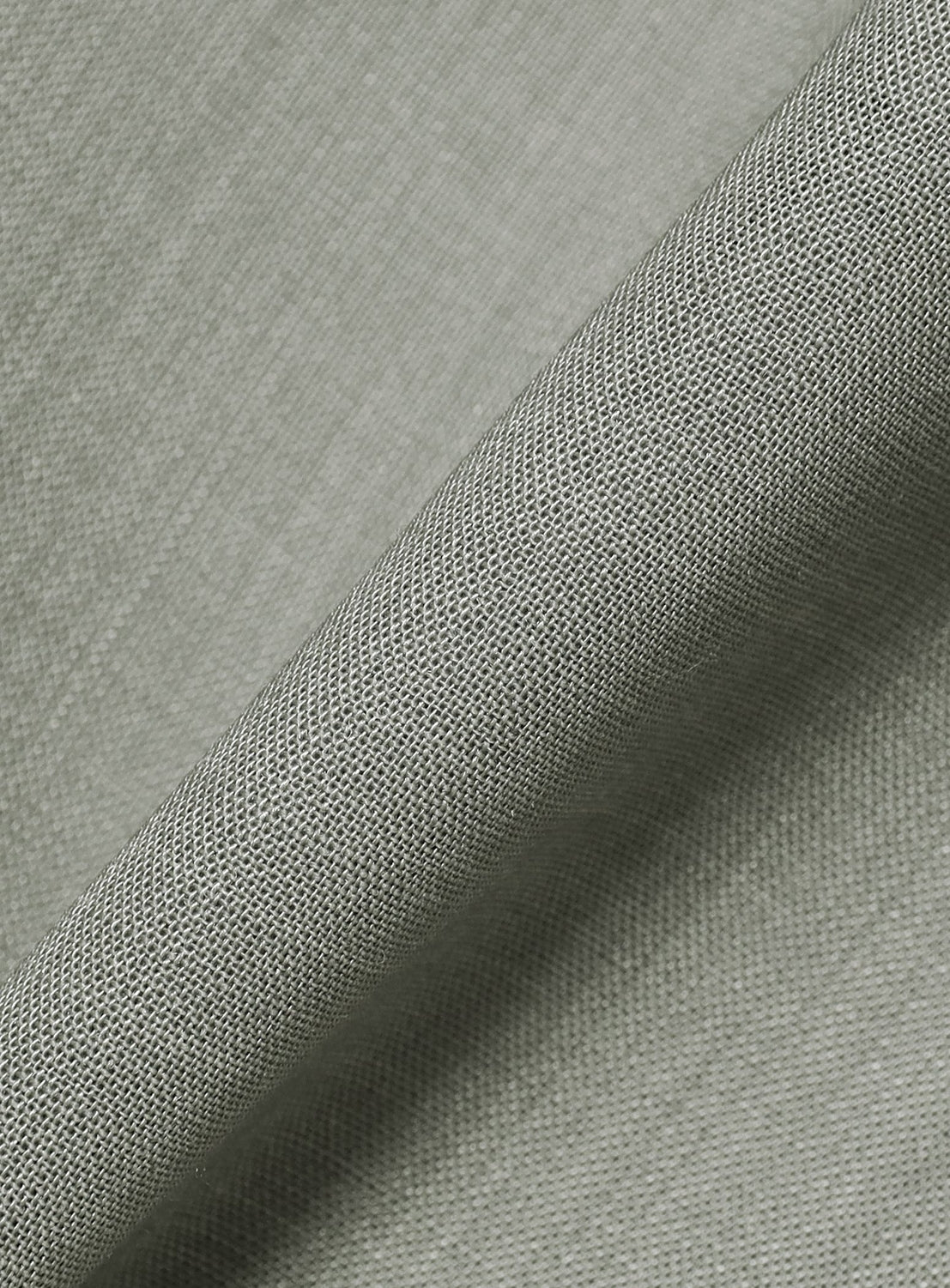 A close-up of light gray linen fabric from the Sheer Tailored Blazer 6S by KANAKO SAKAI, highlighting its woven texture and subtle diagonal lines with a fold running across the image—evoking the refined detailing characteristic of modern menswear blazers.