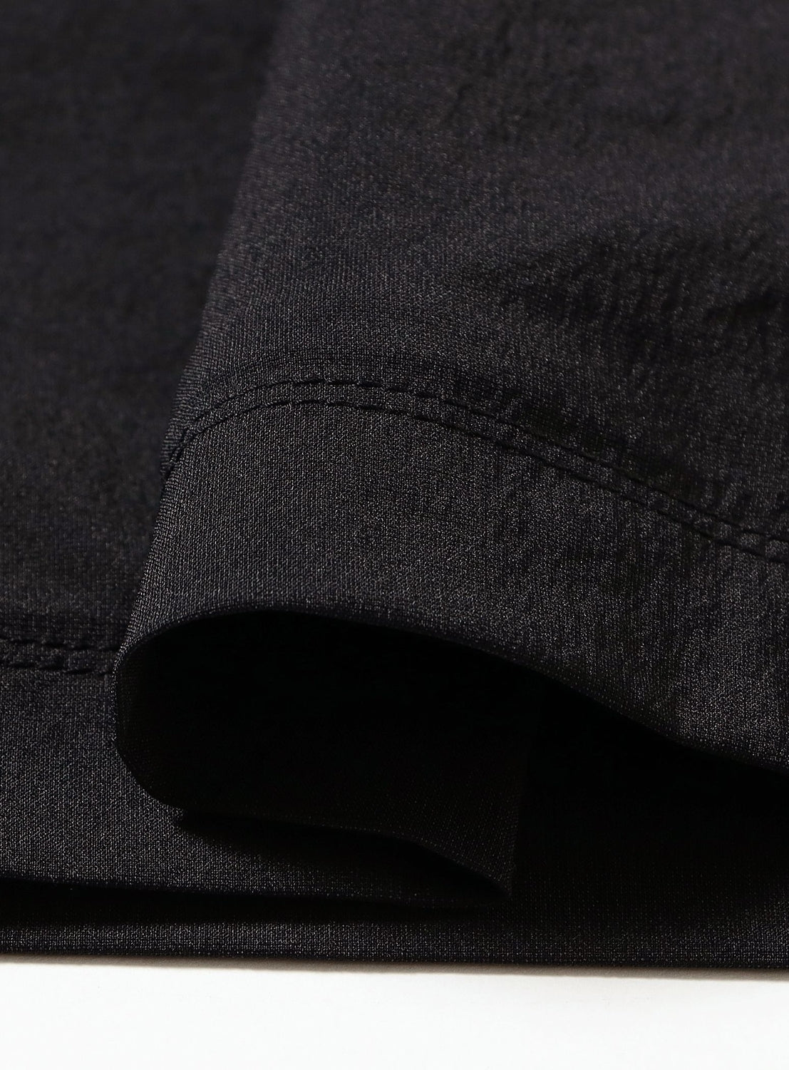 A close-up view of the hem of a black Wallet Pants Resort - Doctoroid garment by TEATORA, neatly folded on a white surface, highlighting the stitching detail and smooth DOCTOROID fabric texture.