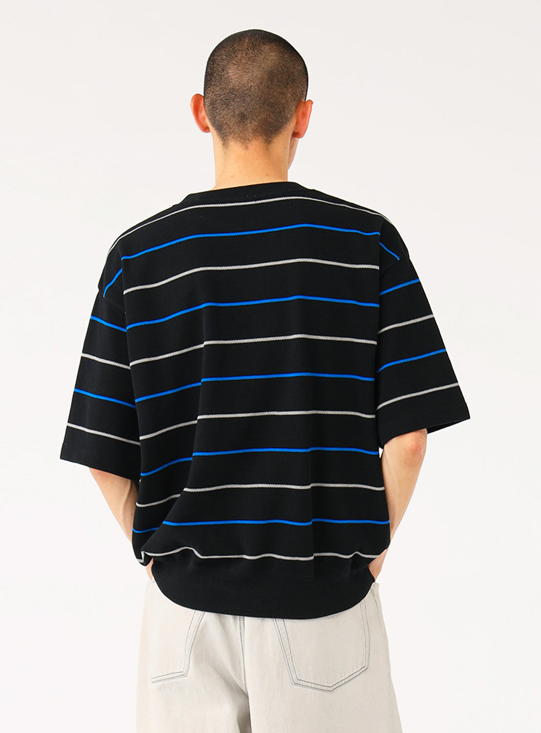 Model wearing a black knit shirt with blue and white stripes, back view, highlighting the continuous pattern.