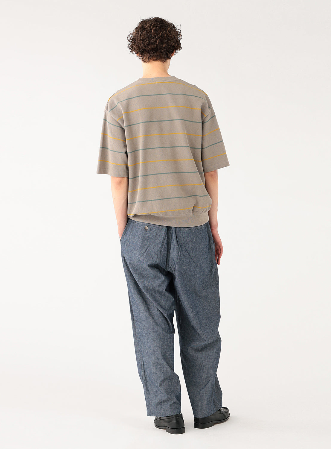 Model wearing a taupe striped knit shirt, back view, highlighting the continuous horizontal stripe pattern.