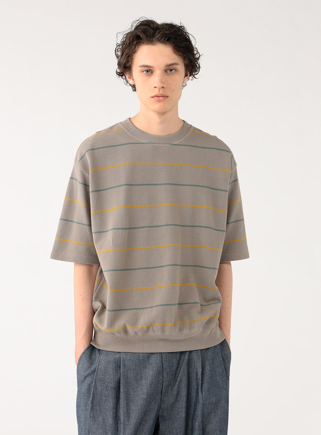 Model in a taupe striped knit shirt and blue pants, full front view, showcasing the casual style.