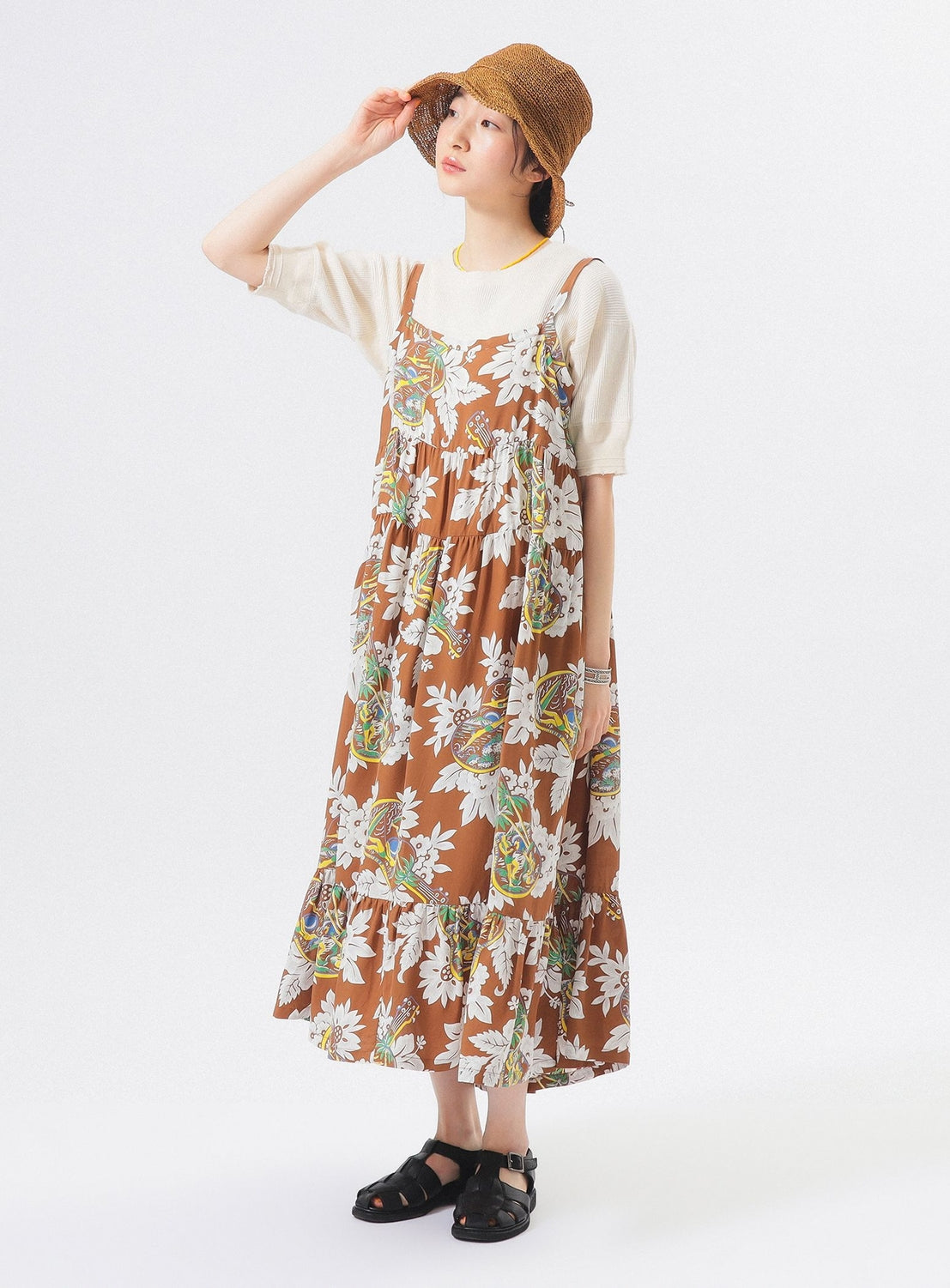 A person models the [Exclusive] SUN SURF Sleeveless Cami Dress by SUN SURF over a white shirt, paired with black sandals and a brown woven hat, posing with one hand touching the hat against a plain white background.
