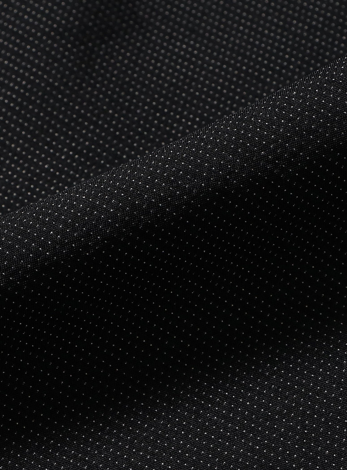 Close-up of a black GEOGRAM textile fabric with a subtle dotted pattern, showing folds and texture under soft lighting—an example of the material used in TEATORA’s Wallet Pants Resort.