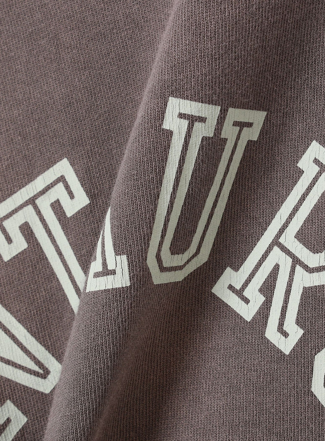 Close-up of the Souvenir T-Shirt by BEAMS featuring brown ribbed cotton jersey and large, outlined white letters. The slightly wrinkled fabric gives it a relaxed, vintage-inspired look.