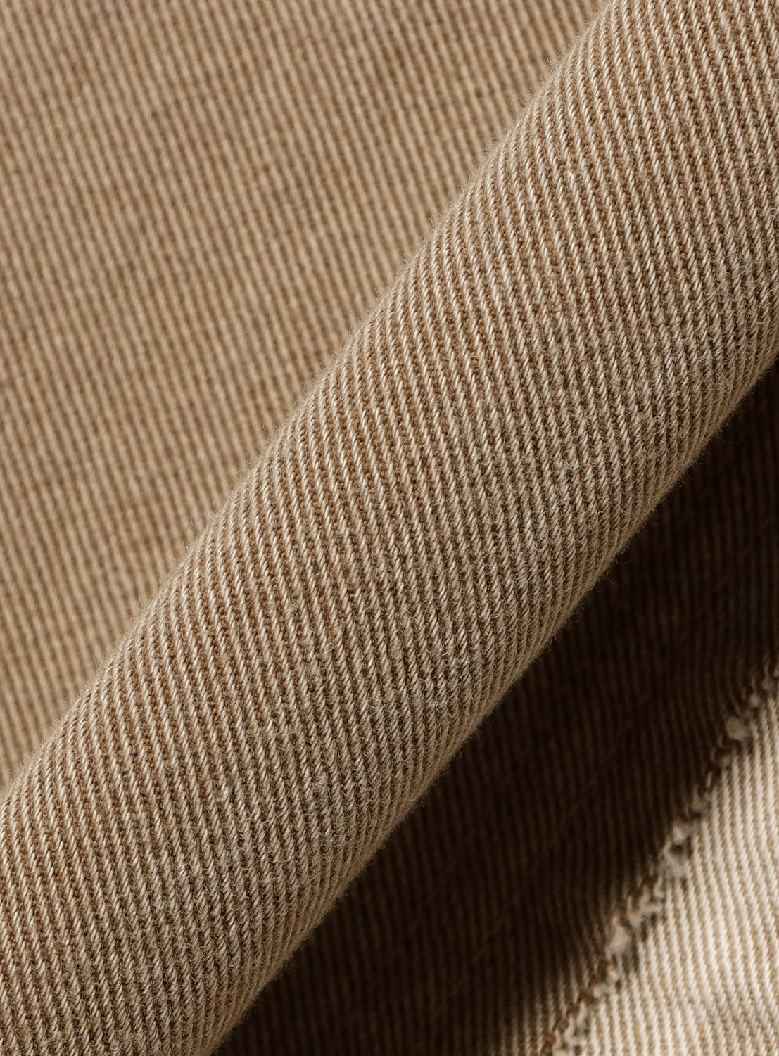 Close-up of INSCRIRE's Colored Denim Straight-Leg Pants in tan, highlighting the diagonal twill weave, a neatly folded edge, and subtle frayed detailing.