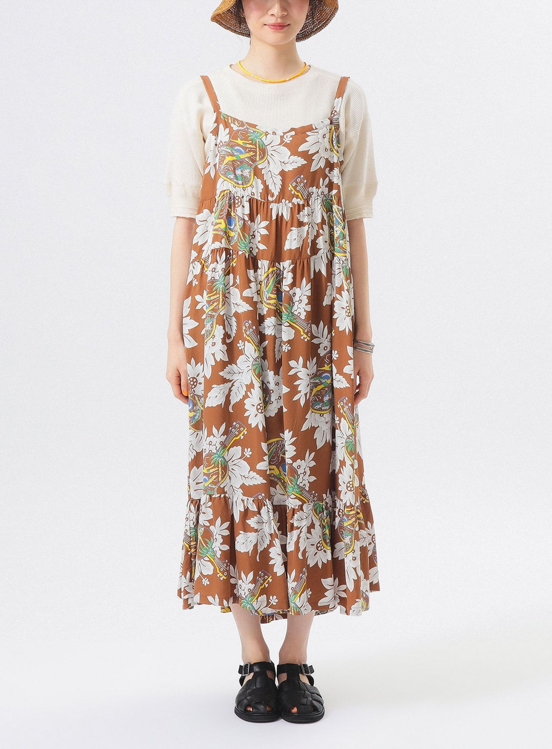 Wearing the [Exclusive] SUN SURF Sleeveless Cami Dress by SUN SURF over a white short-sleeve top, paired with a straw hat, black sandals, yellow necklace, and bracelets, someone stands against a white background.