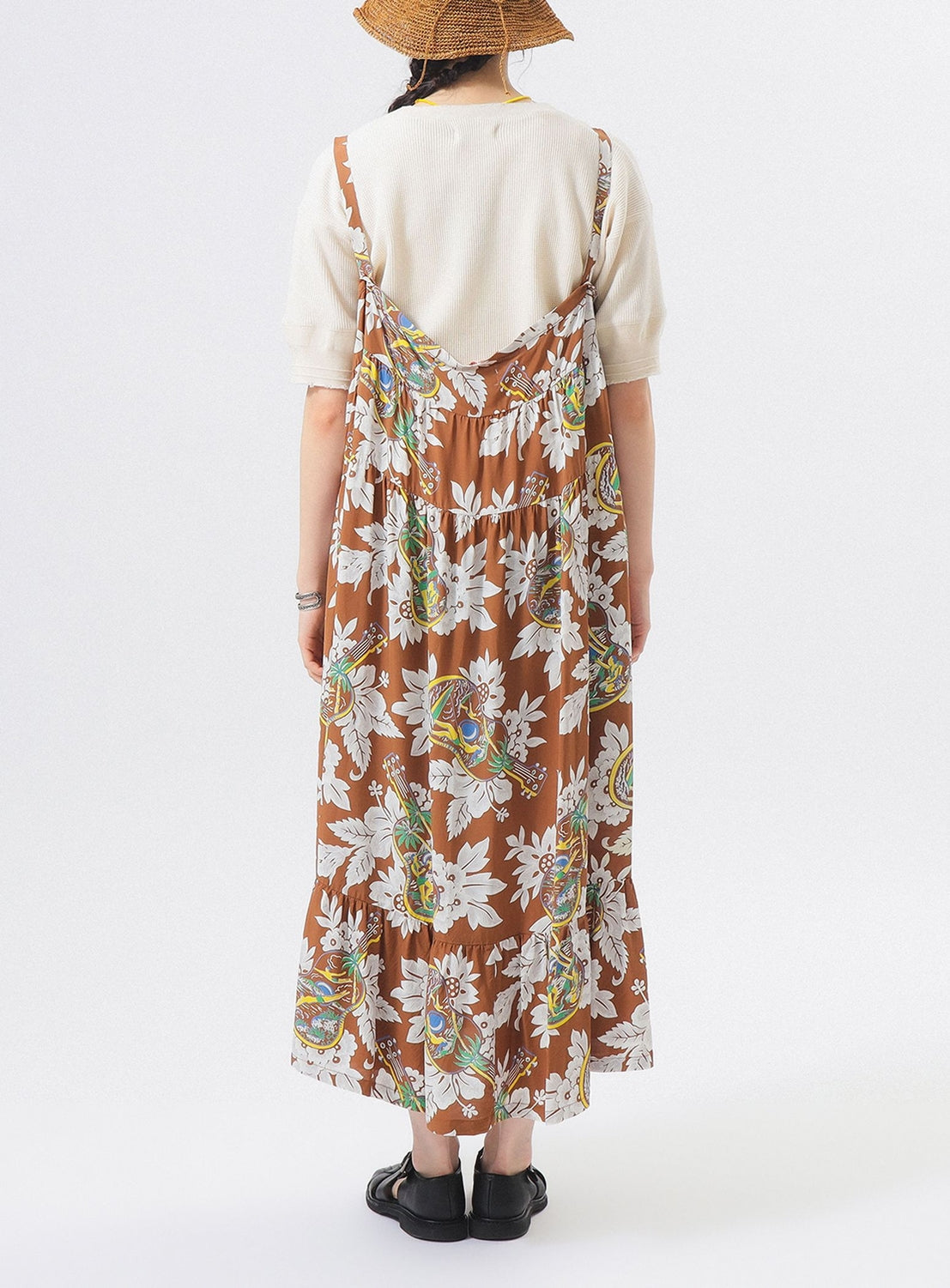 A person stands with their back to the camera against a white background, wearing the SUN SURF [Exclusive] Sleeveless Cami Dress over a short-sleeved white top, paired with black shoes and a brown hat.