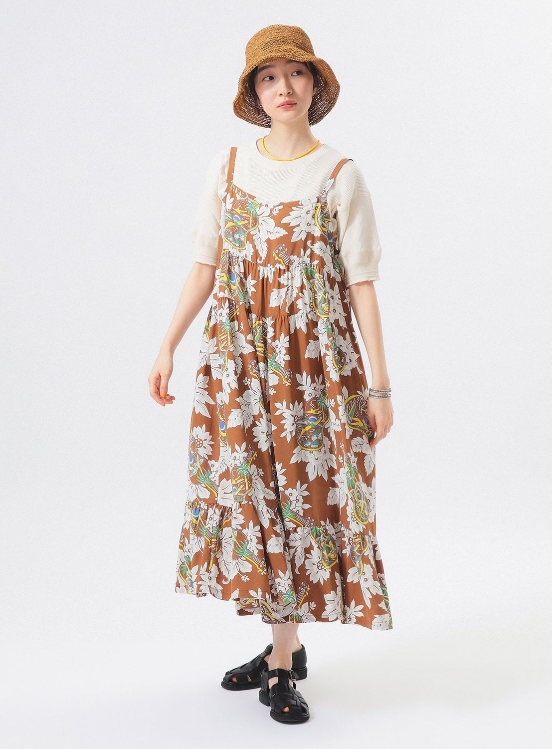 A woman models the [Exclusive] SUN SURF Sleeveless Cami Dress by SUN SURF over a white shirt, styled with black sandals and a brown woven hat, standing against a plain white background and looking relaxed.
