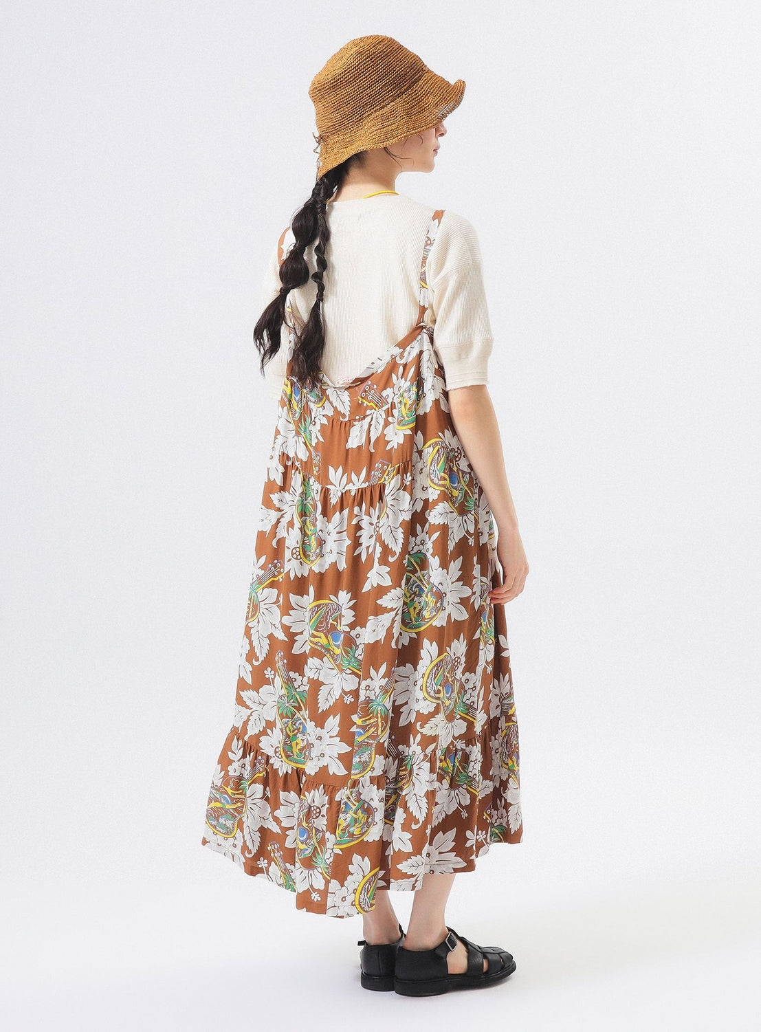 A person with long dark braided hair wears the [Exclusive] SUN SURF Sleeveless Cami Dress by SUN SURF, paired with a tan hat, white short-sleeve top, and black sandals, standing and facing away from the camera against a white background.