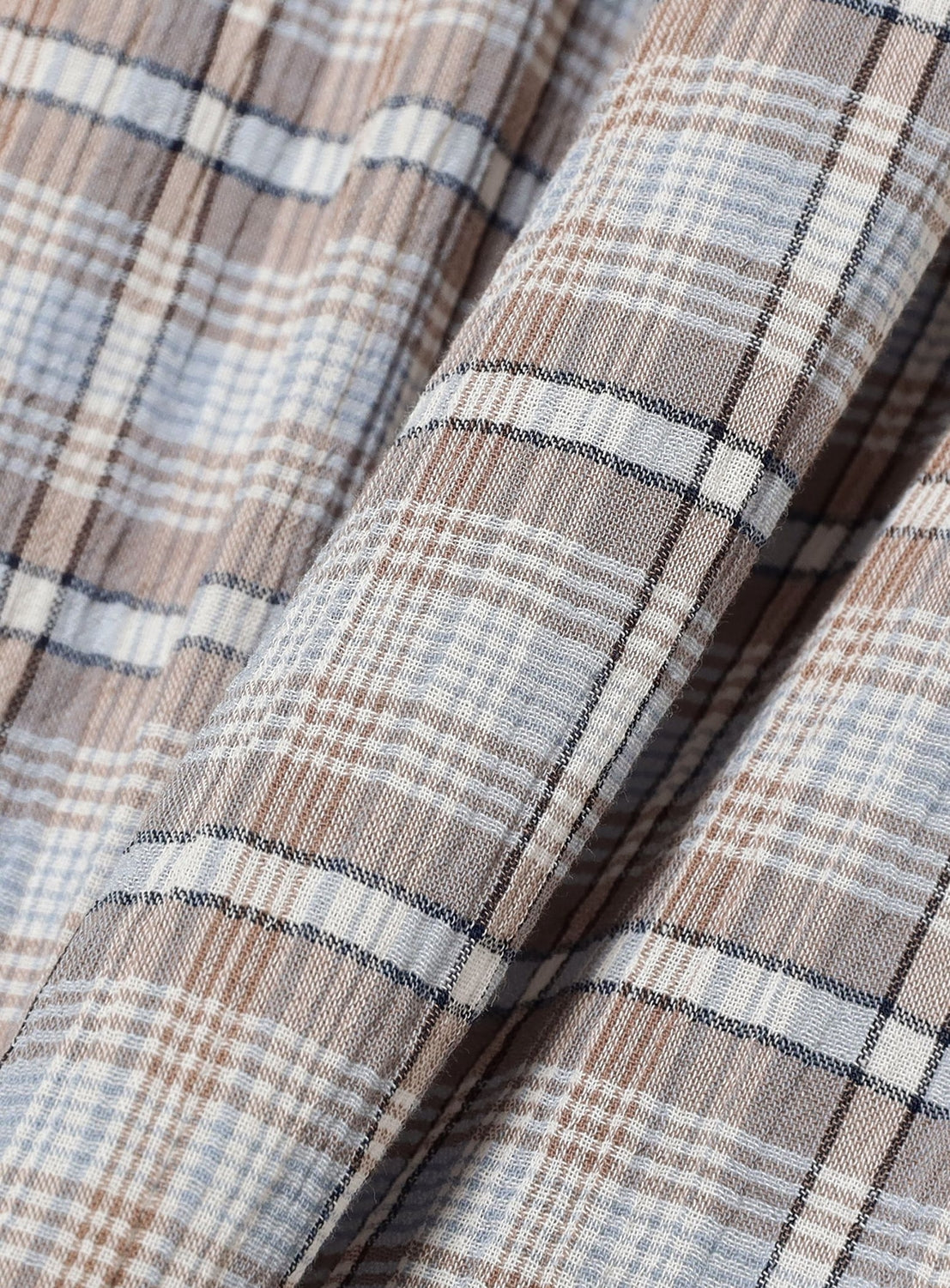Close-up of beige, white, and light blue plaid fabric with diagonal folds. The intersecting lines in soft, muted tones form a classic check pattern characteristic of BEAMS BOY. This lightweight material is featured in the Check Tiered Skirt by BEAMS BOY, making it an ideal choice for those seeking both style and comfort.