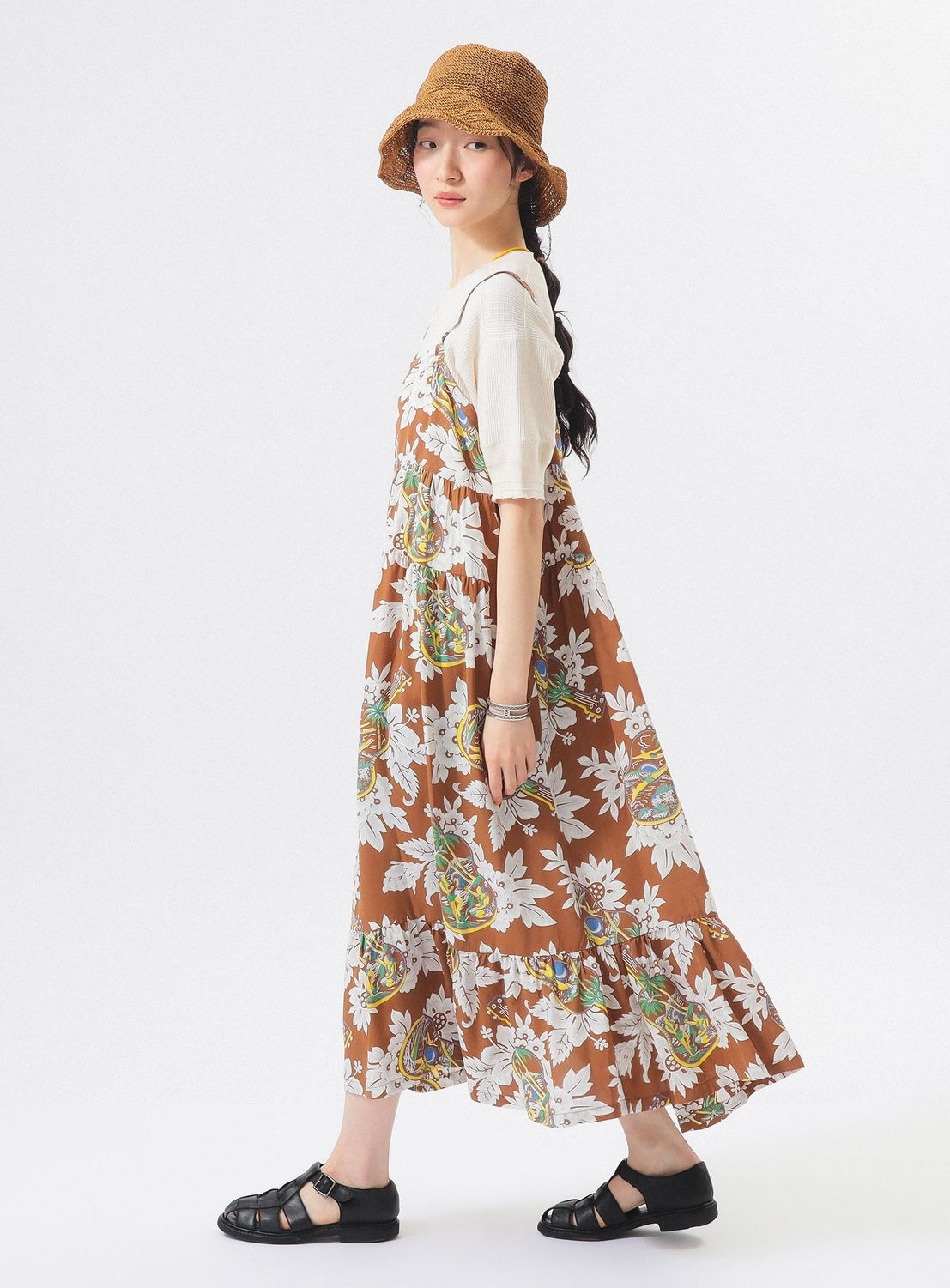A woman with long dark hair wears the [Exclusive] SUN SURF Sleeveless Cami Dress by SUN SURF, styled with a tan hat, cream short-sleeve shirt, and black sandals. She stands against a white background in this resort-inspired look.