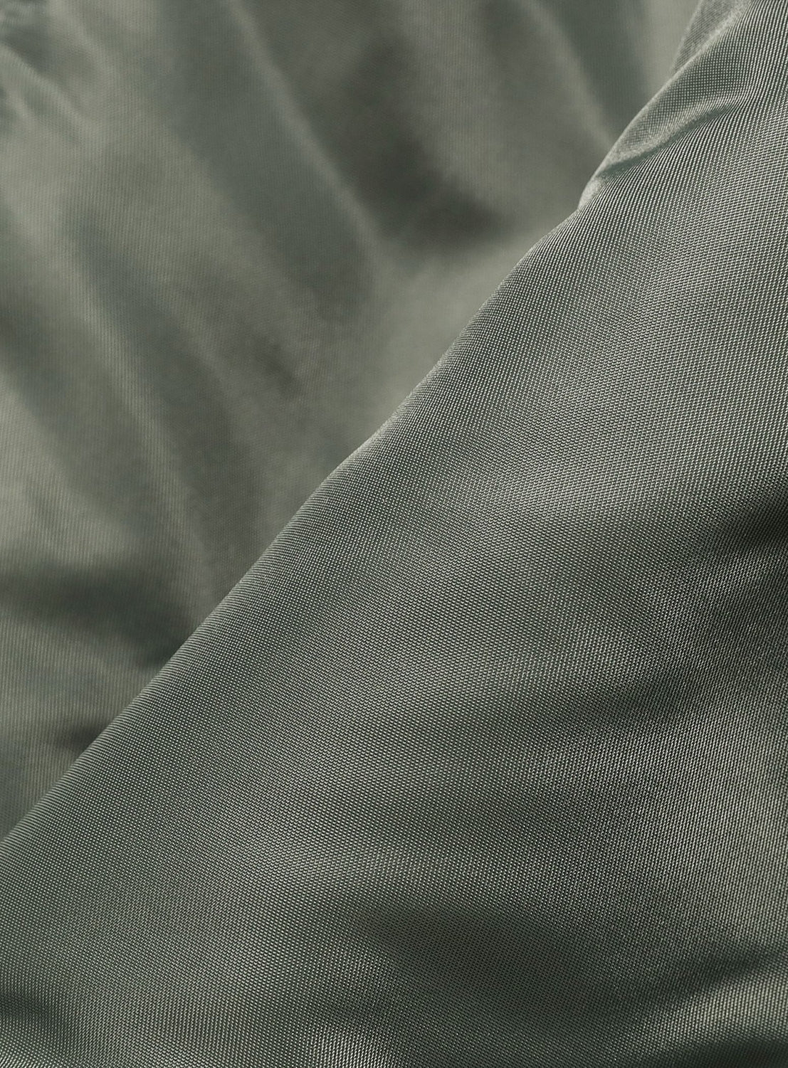 Close-up of the smooth, sage green fabric used in BUZZ RICKSON’s Type N-3B Coat, featuring soft folds and a subtle sheen that highlights the fine texture and distinctive diagonal weave pattern typical of cold-weather jackets.