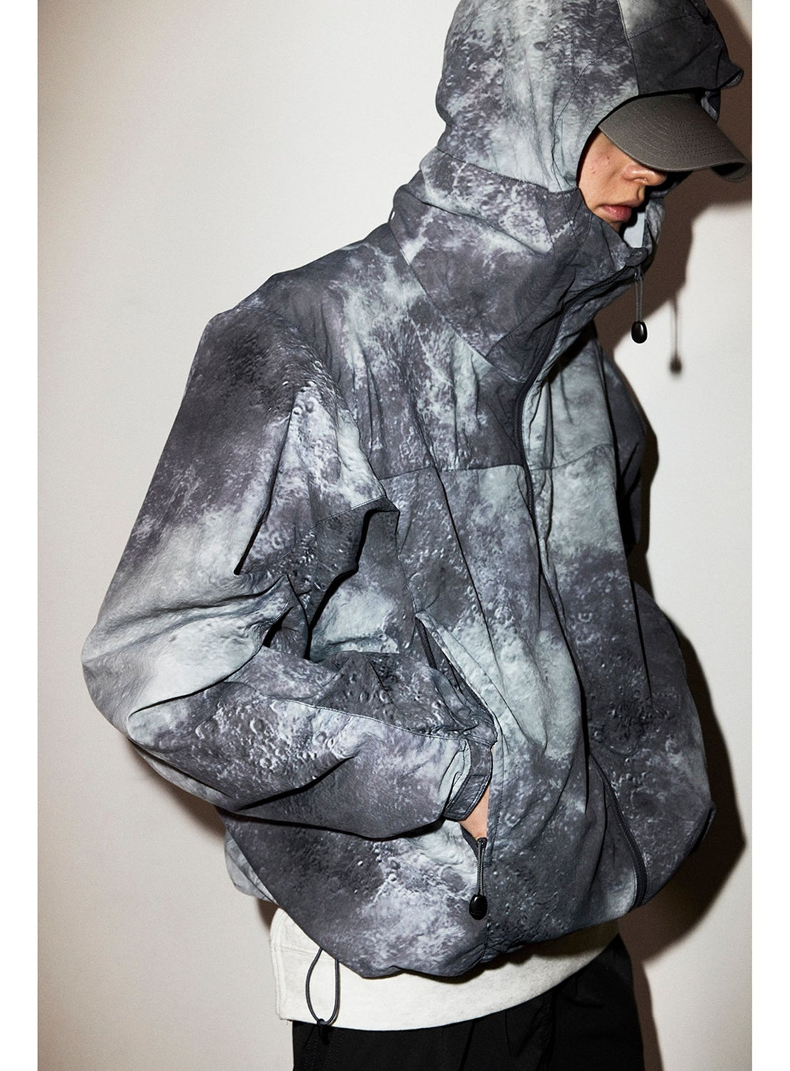 A person wearing a BEAMS Print Zip Hooded Jacket featuring a lightweight, zip-up technical design with a grey and black lunar surface print.
