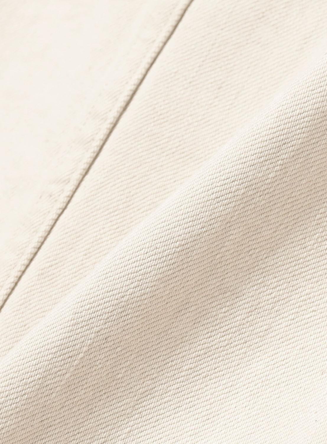 Close-up of cream-colored fabric with a diagonal weave, similar to Okayama denim, highlights the texture and folds of the SUGARHILL Tattoo Flash Print Denim Jacket.