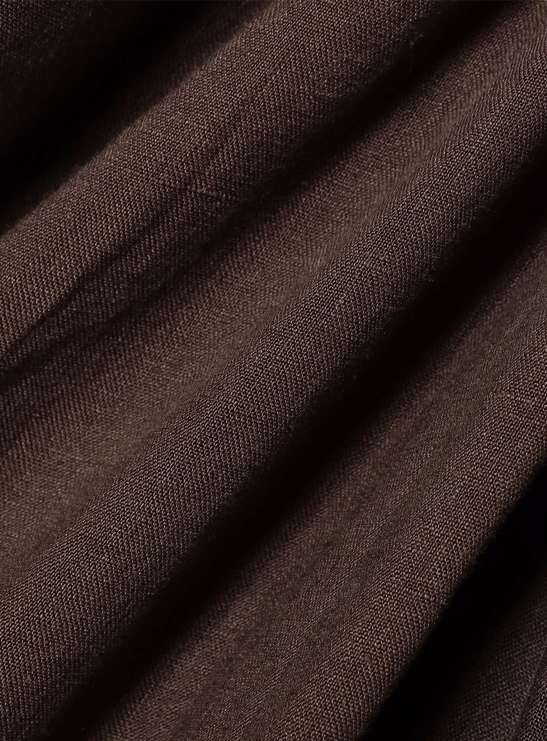 Close-up of the enrica Linen 2-Way All-in-One Jumpsuit fabric in brown, highlighting its visible diagonal weave pattern, soft folds, and natural shadows that showcase the texture.
