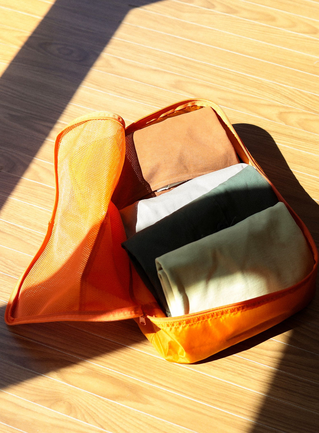 Orange mesh pouch with folded clothes on a wooden surface