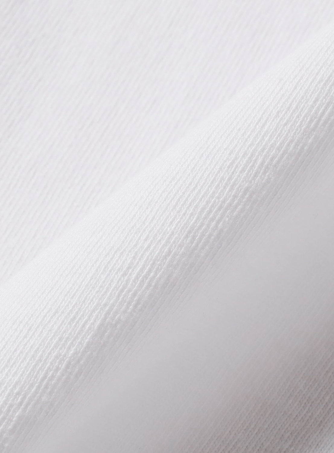 Close-up of a white FACE Graphic T-Shirt by BEAMS T, highlighting its fine texture and diagonal weave. Lighting accentuates the soft, smooth surface and subtle shadows—part of a special anniversary collaboration.