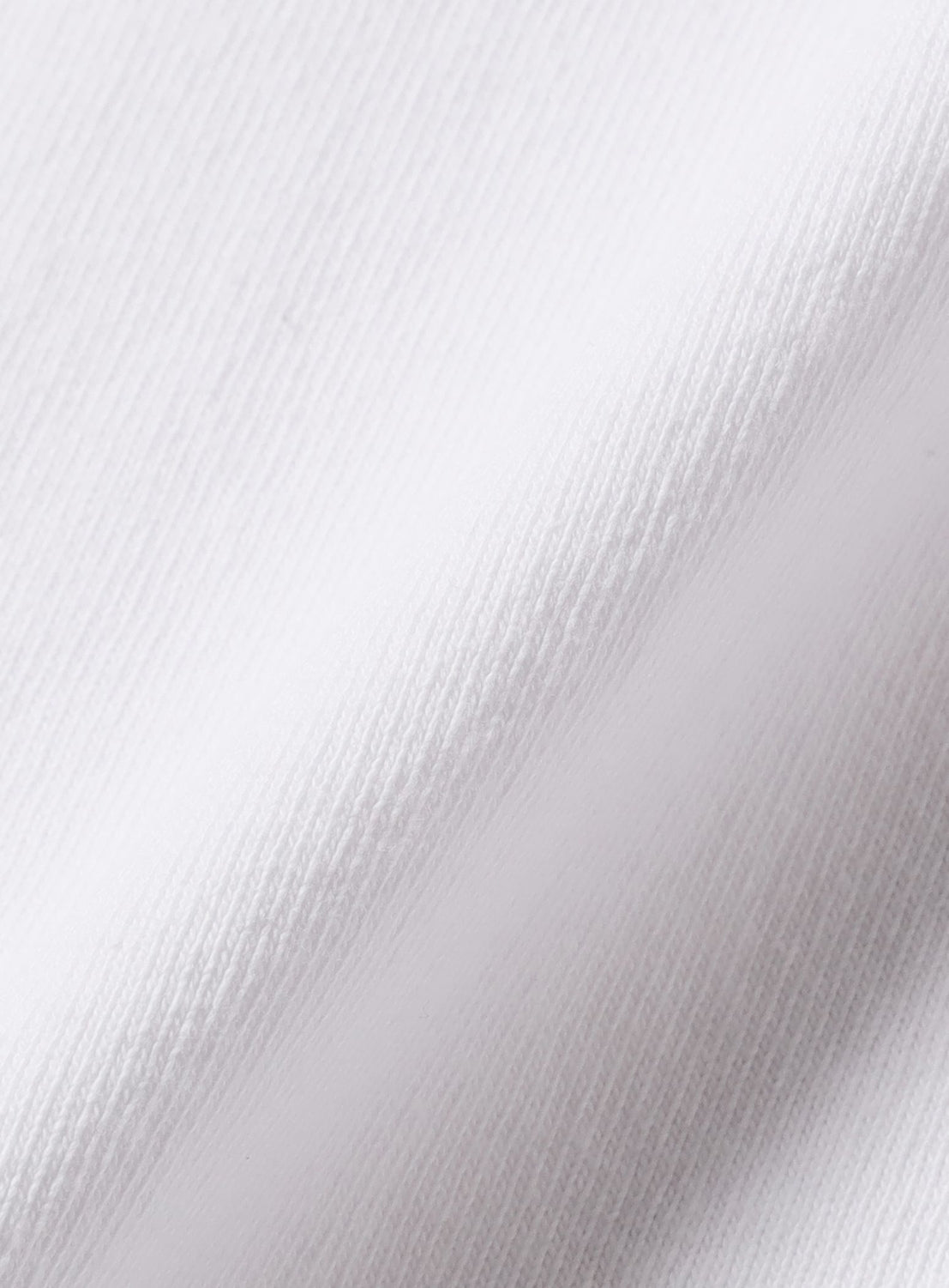 Close-up of the YU NAGABA T-shirt by BEAMS T, showing white fabric with a subtle diagonal weave and soft texture. Gentle folds and shadows highlight this special edition.