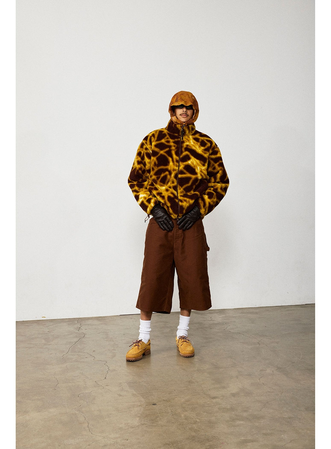 Person wearing a BEAMS Print Zip Hooded Jacket with a brown and yellow giraffe-like pattern, brown knee-length shorts, black gloves, white socks, and tan shoes.