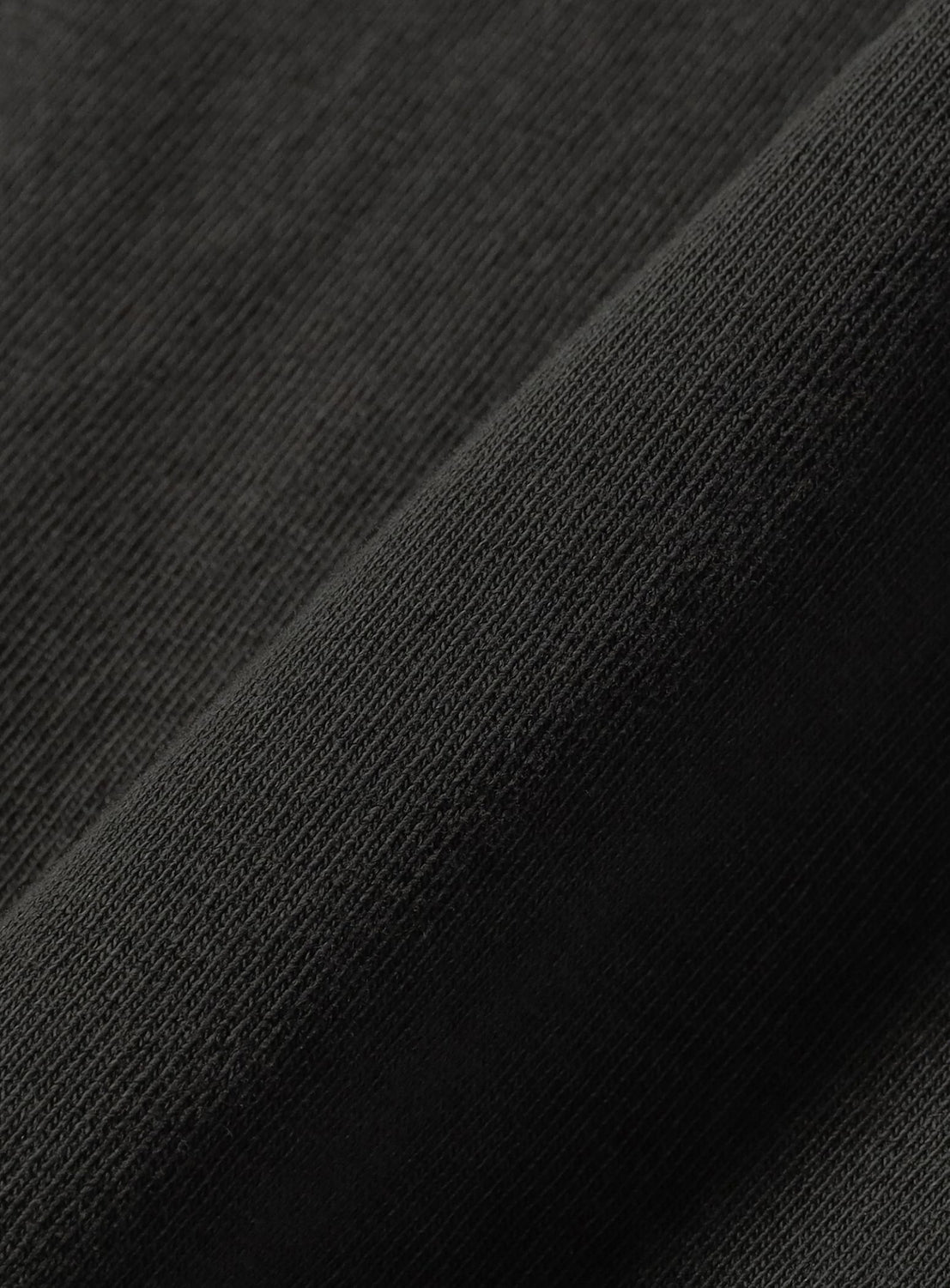 Close-up of the JUN OSON T-shirt by BEAMS T in dark gray or black heavyweight jersey, showcasing its soft texture and visible knit weave with a folded section.
