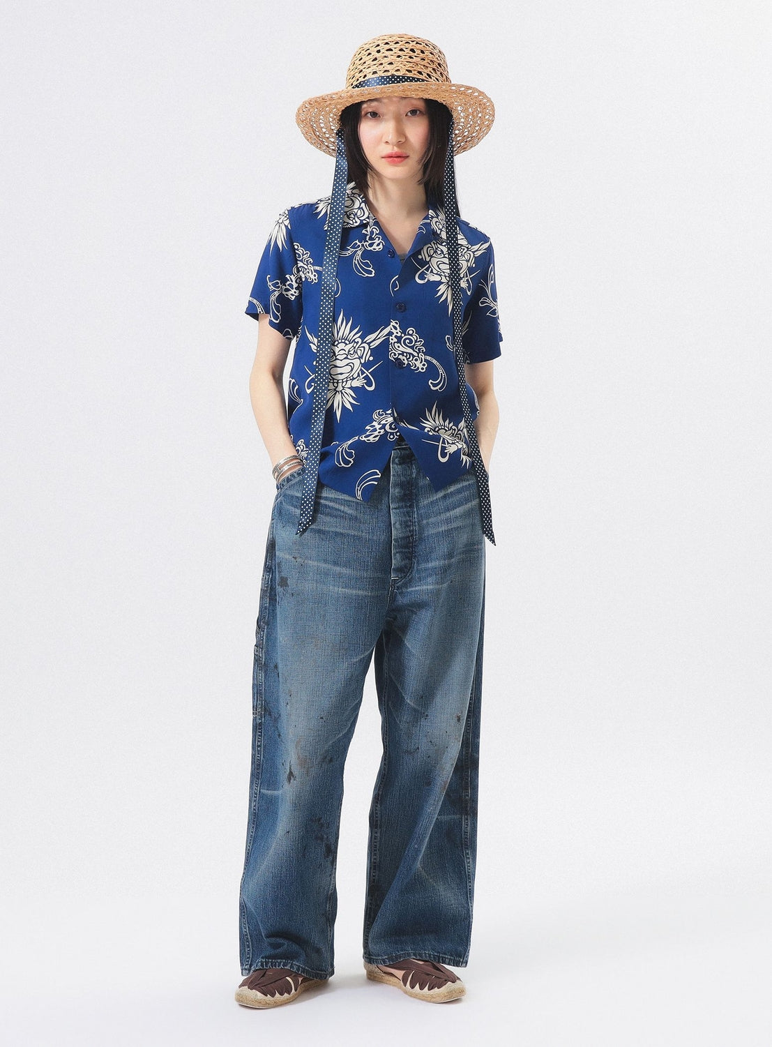 Wearing the [Exclusive] SUN SURF x BEAMS BOY Open Collar Shirt by SUN SURF, a person pairs it with a straw hat, wide-leg faded jeans, and brown shoes against a white background, showcasing a relaxed Hawaiian-inspired style.
