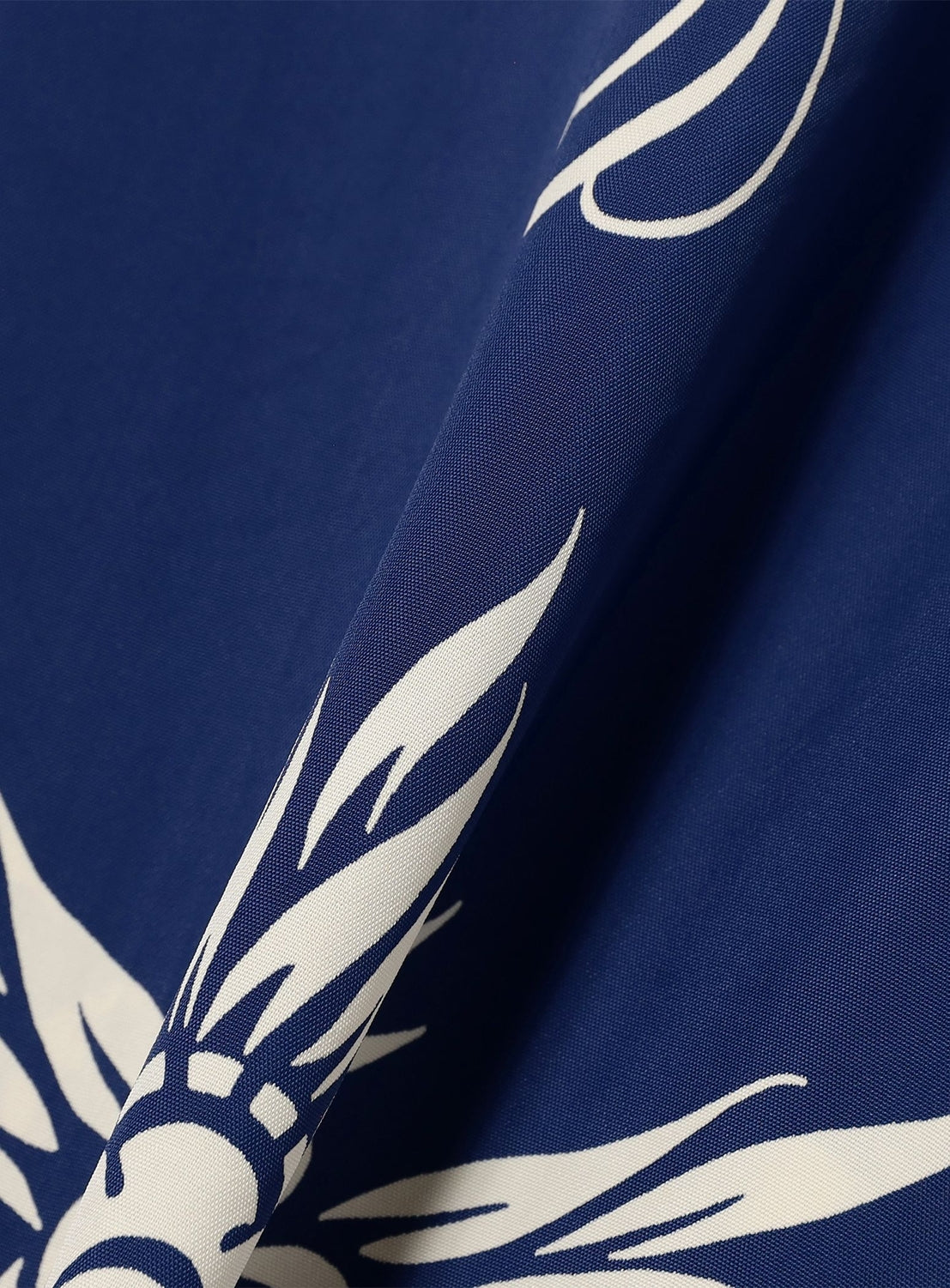 A close-up of blue fabric with a white abstract floral or feather pattern and subtle texture, reflecting vintage aloha shirt vibes from the [Exclusive] SUN SURF x BEAMS BOY Open Collar Shirt by SUN SURF.