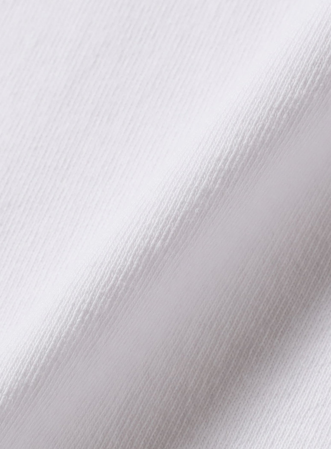 Close-up of the KYNE T-shirt by BEAMS T in heavyweight jersey, highlighting its fine, soft texture and subtle diagonal ribbing. Slight folds in the fabric create gentle shadow along the crease.