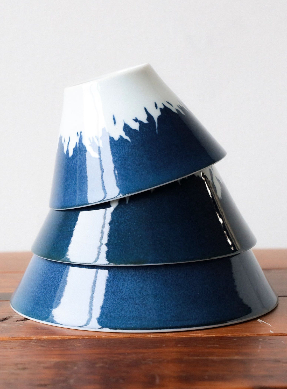 Stack of blue ceramic bowls on a wooden surface with a white background