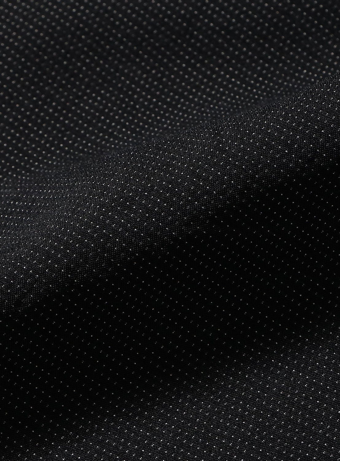 Close-up of black GEOGRAM textile fabric with a subtle pattern of tiny white dots, slightly folded to showcase its texture and drape—an ideal detail featured in TEATORA’s Wallet Shorts Resort, which includes a discreet Security Cargo Pocket.
