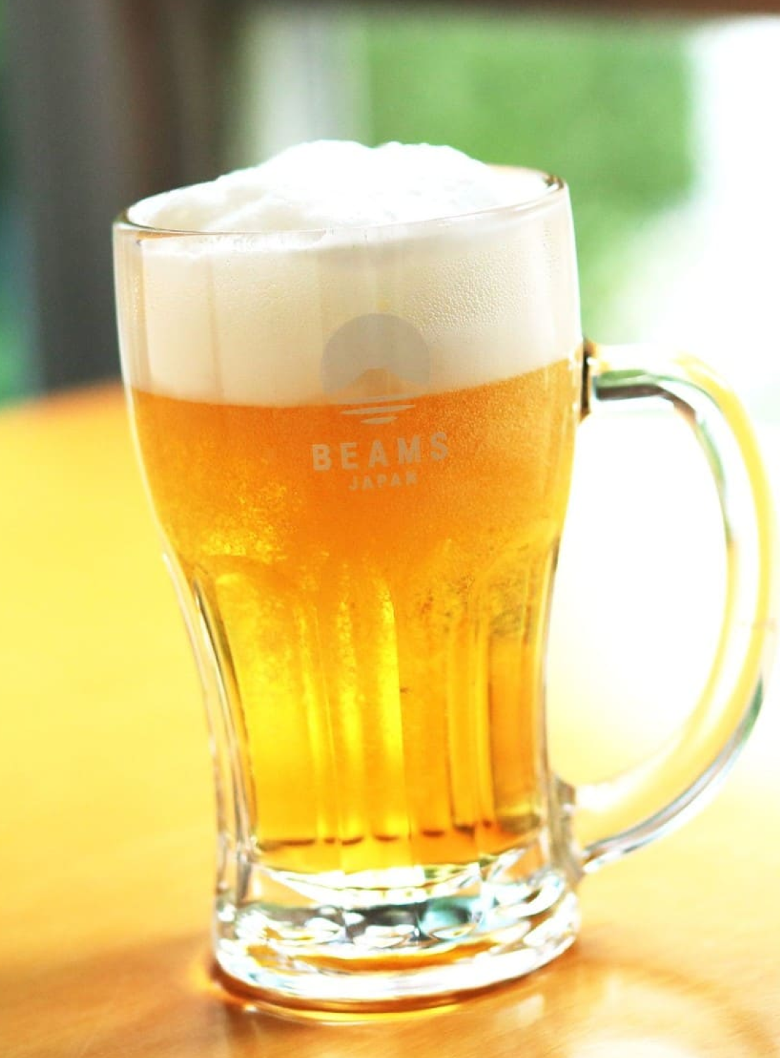 Glass of beer with foam on a wooden surface, featuring the 'BEAMS' brand.