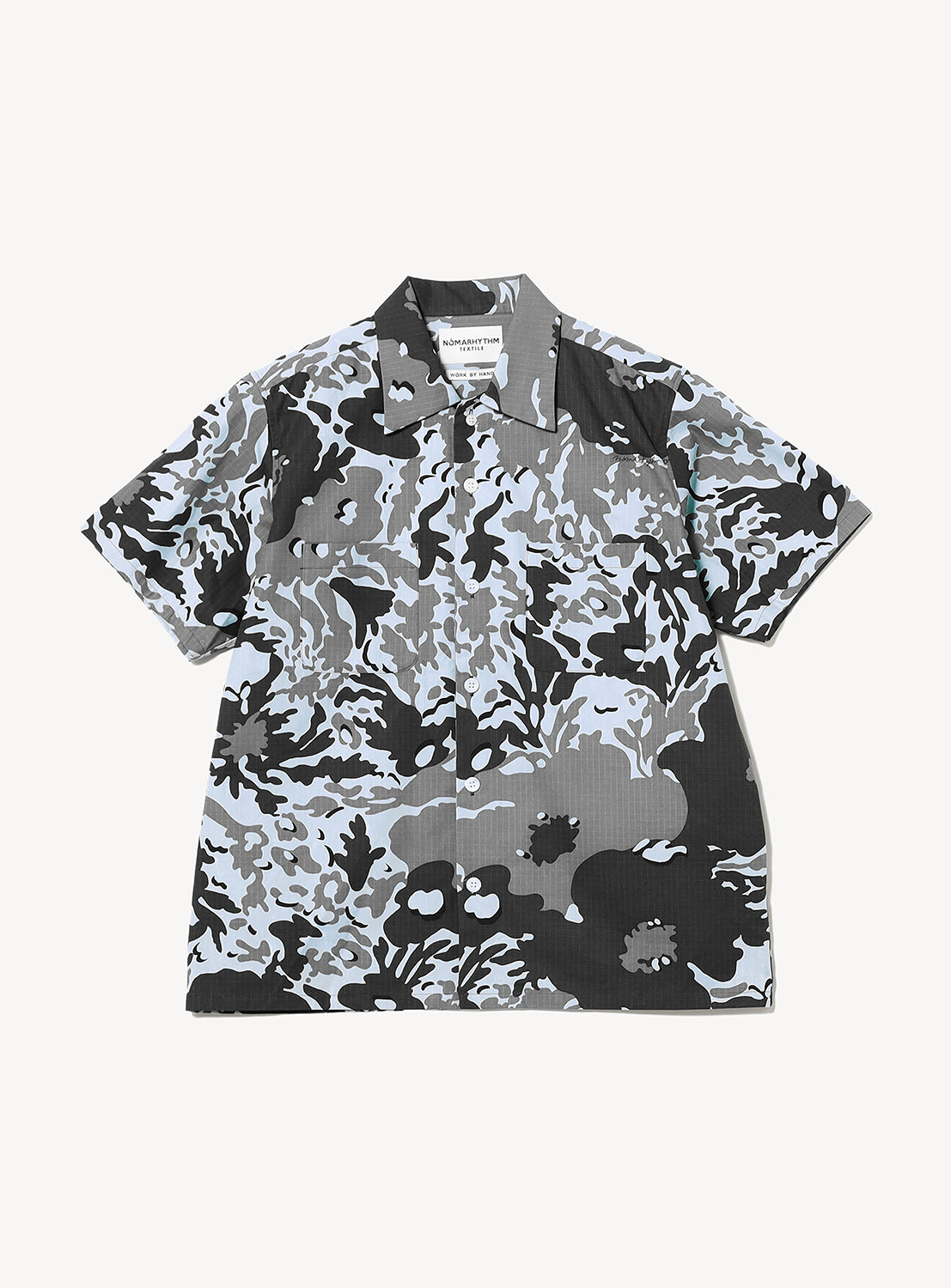 The Camo Flower Open Shirt from NOMARHYTHM TEXTILE is a short-sleeve button-up with an abstract camouflage floral pattern in gray, black, and white. Featuring two chest pockets and a pointed collar, this shirt is crafted in Japan from lightweight cotton for superior comfort and quality.