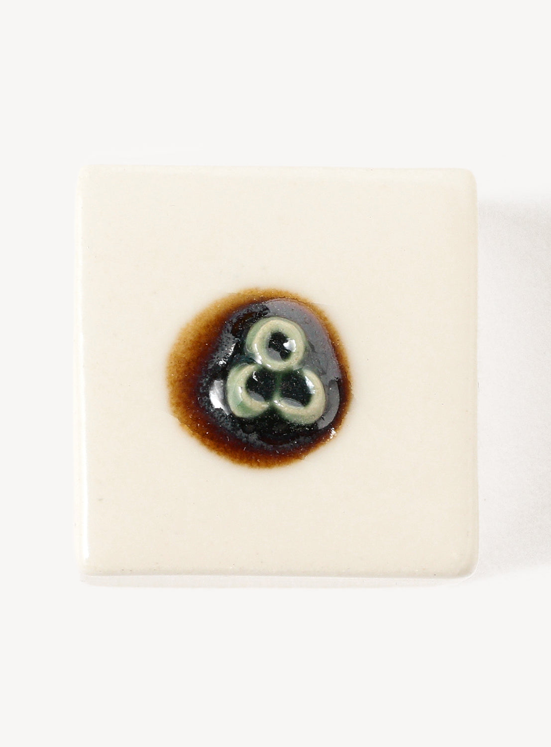 White hexagonal chopstick rest with a small black and brown design on a white background