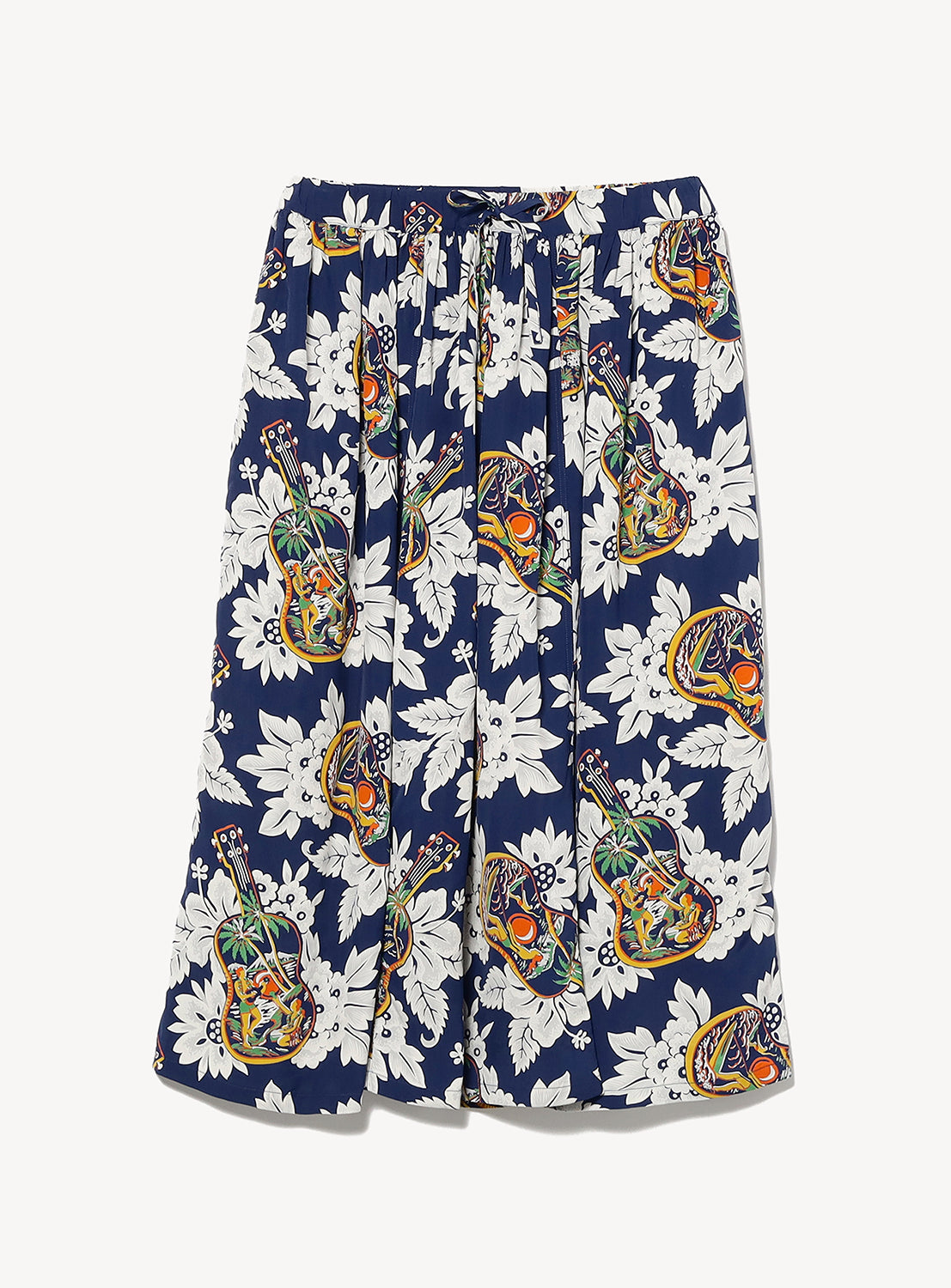 The [Exclusive] SUN SURF x BEAMS BOY Aloha Gathered Long Skirt by SUN SURF features a blue base with bold white florals and colorful pineapple motifs, creating a vintage Hawaiian look, shown flat on a white surface.