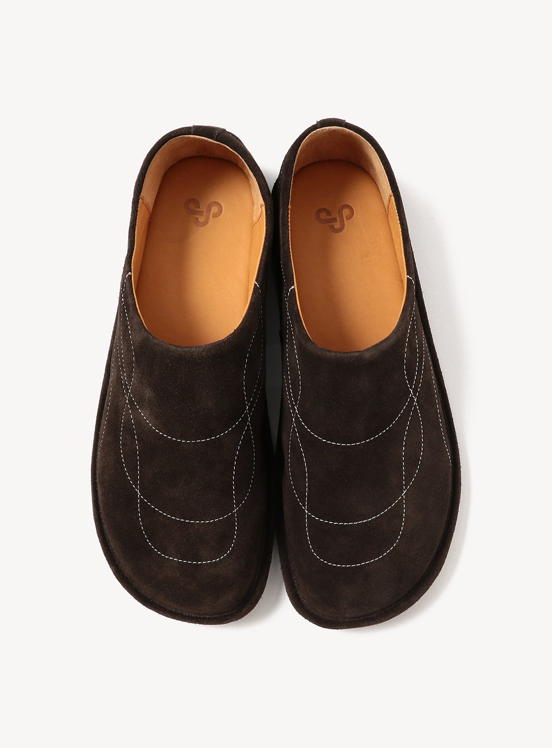The OAO Sunlight Orb, a pair of dark brown suede slip-on shoes with light brown leather insoles and white decorative stitching, features a sculptural design inspired by Isamu Noguchi, shown from above on a white background.
