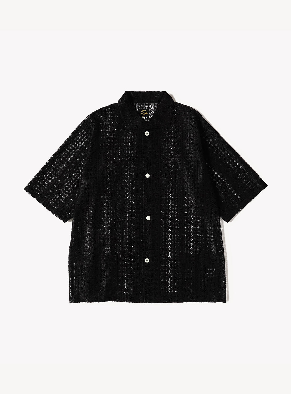 Front view of a black short-sleeve lace shirt featuring a relaxed boxy silhouette, open collar, and front button closure with contrasting white buttons. The sheer Raschel lace fabric showcases an intricate vertical knit pattern, creating a lightweight and breathable look.