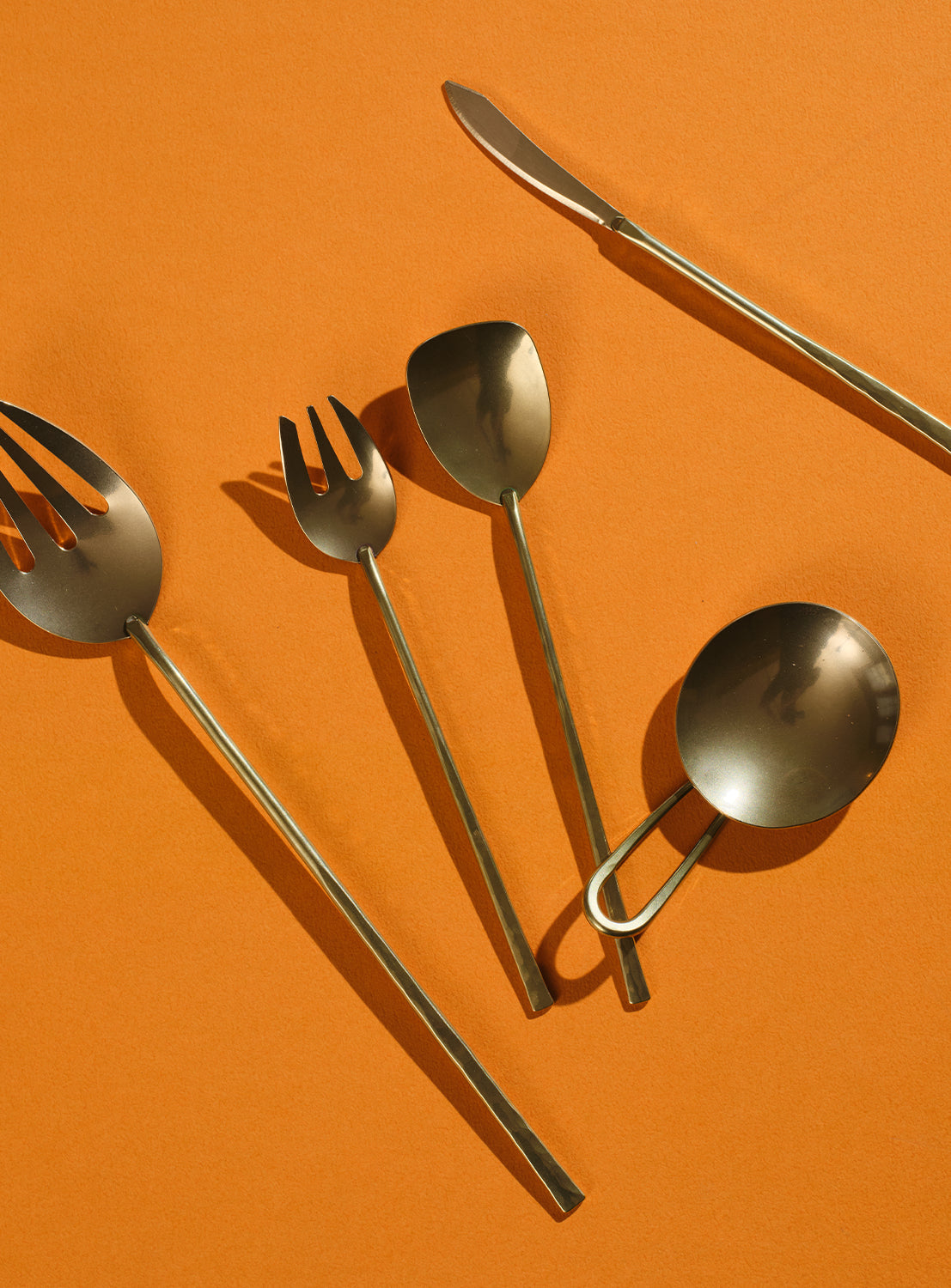 Set of gold-colored cutlery including forks and spoons on an orange background.