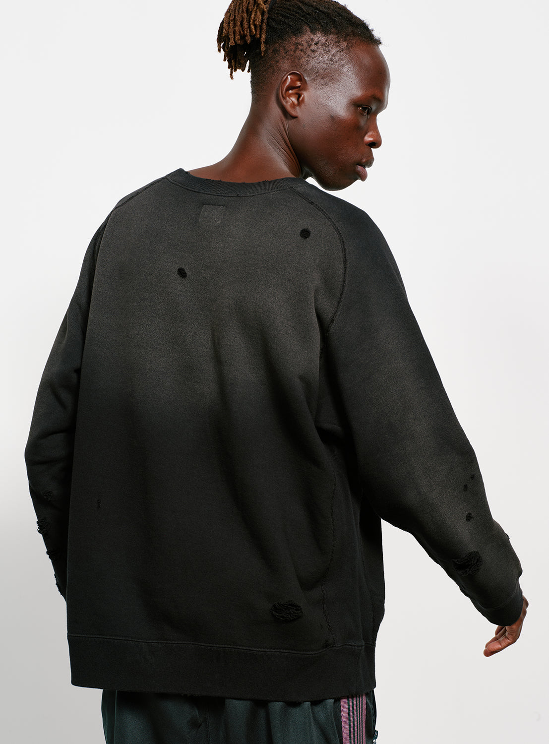 Backside of a model wearing a black distressed and faded sweatshirt with a butterfly design in white. 