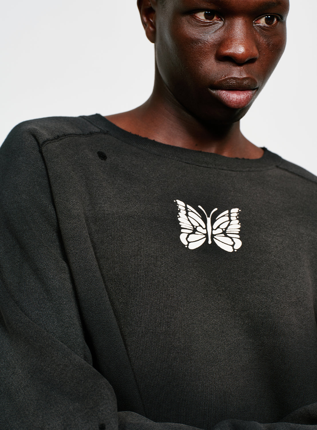 Close up of a model wearing a black distressed and faded sweatshirt with a butterfly design in white. 