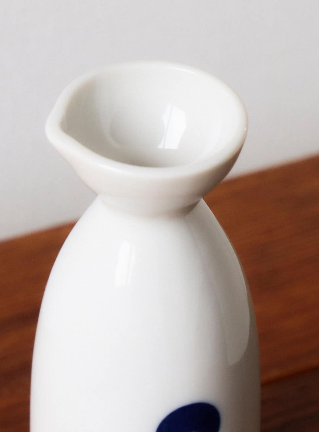 A close-up of the BEAMS JAPAN Sake Bottle 360ML, a minimalist white ceramic tokkuri by BEAMS JAPAN with a small spout, placed on a wooden surface against a light-colored background.